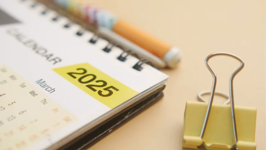 Foto aproximada de calendário espiral aberto na página de março, com o ano 2025 destacado em etiqueta amarela ao lado de um lápis