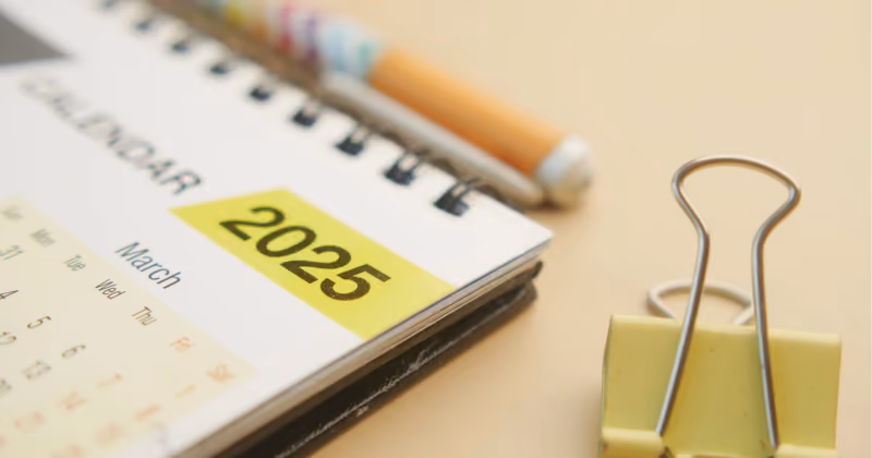 Foto aproximada de calendário espiral aberto na página de março, com o ano 2025 destacado em etiqueta amarela ao lado de um lápis