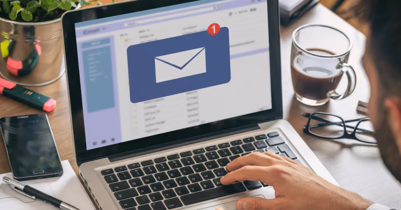 Foto de um homem usando notebook com a caixa de entrada aberta e um grande ícone de envelope na tela, ao lado de um café