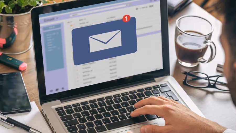Foto de um homem usando notebook com a caixa de entrada aberta e um grande ícone de envelope na tela, ao lado de um café