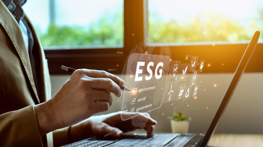 Foto de mãos em um laptop tocando painel holográfico com a sigla ESG e os rótulos environment, social e governance