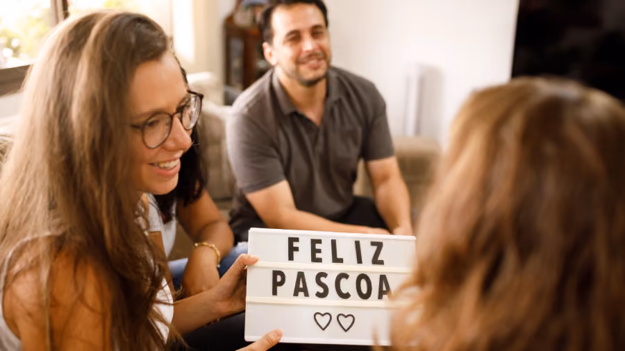 Foto de três pessoas conversando numa sala, uma delas segurando um quadro luminoso com os dizeres Feliz Páscoa e dois corações